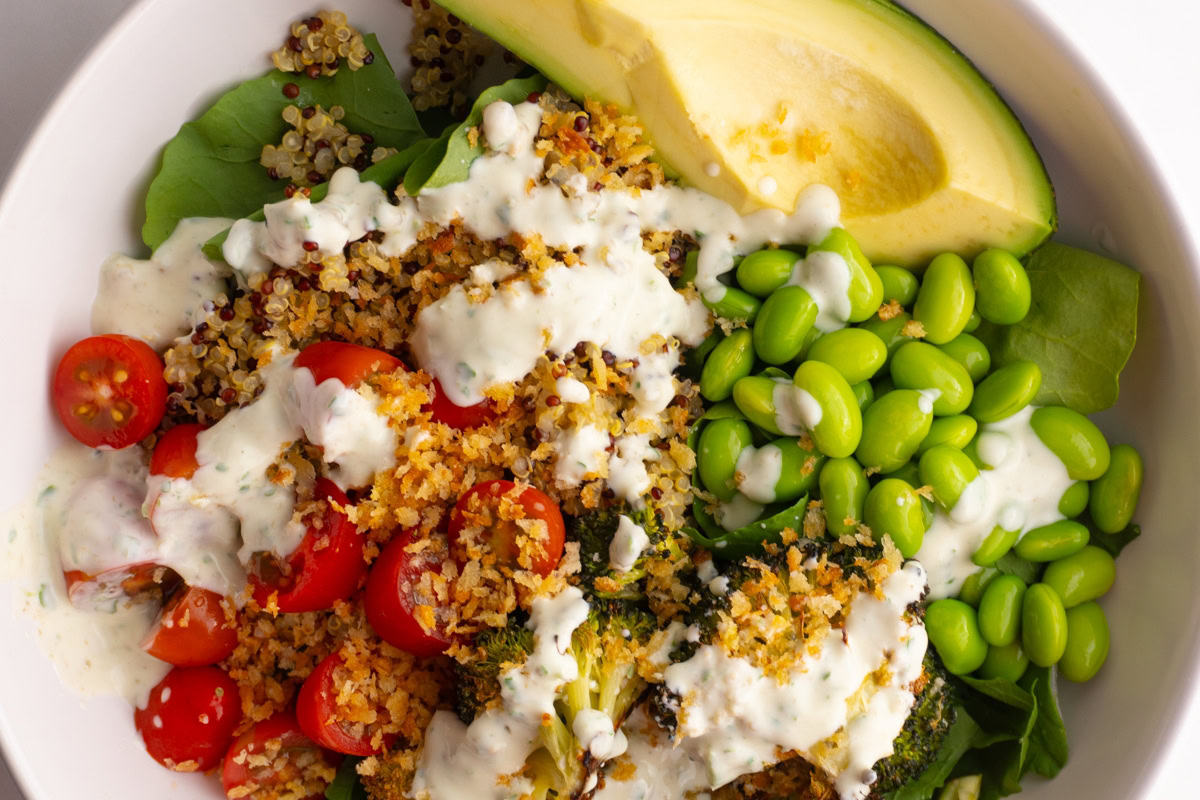 Close up of a green goddess bowl with lots of veggies topped with breadcrumbs and sauce.