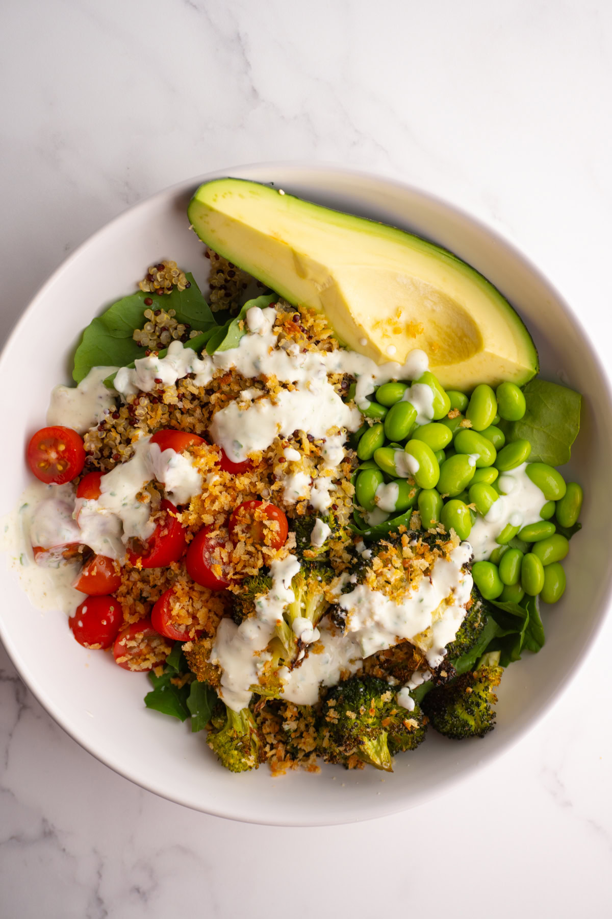 Green goddess bowl with quinoa, avocado, cherry tomatoes, broccoli, and creamy dressing.