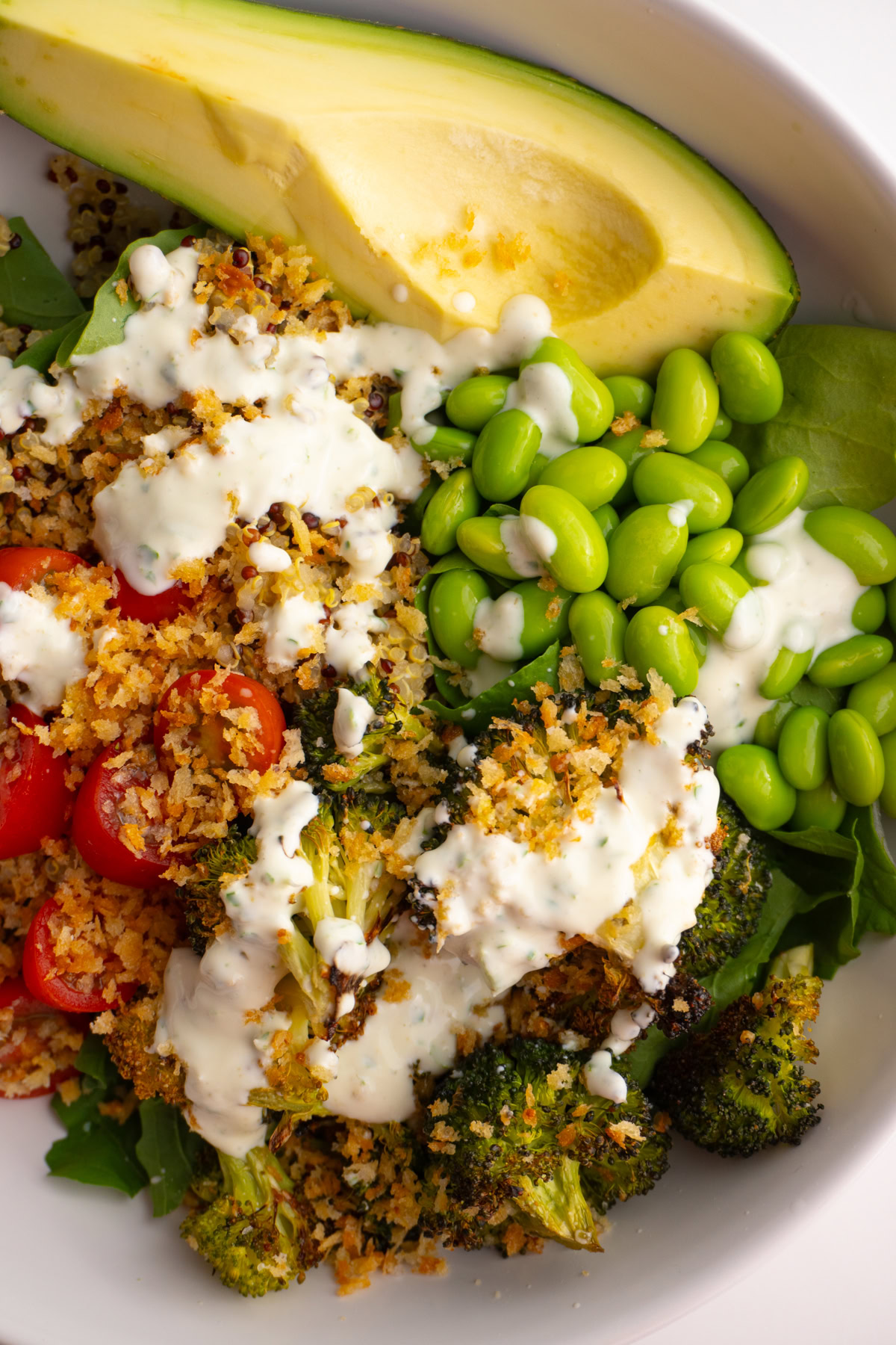 Close up of green goddess bowl with broccoli, tomatoes, edamame, and avocado with sauce on top.
