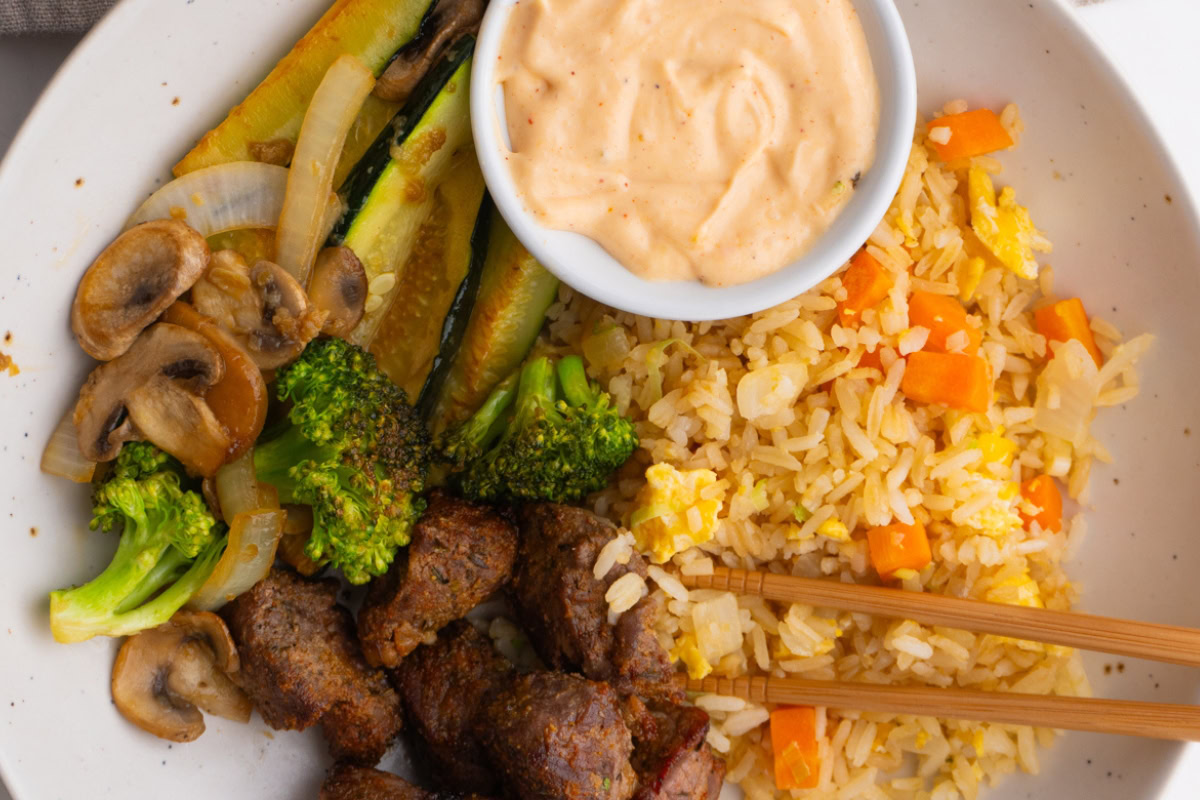 Close up of hibachi steak bowls with sauce on the side.