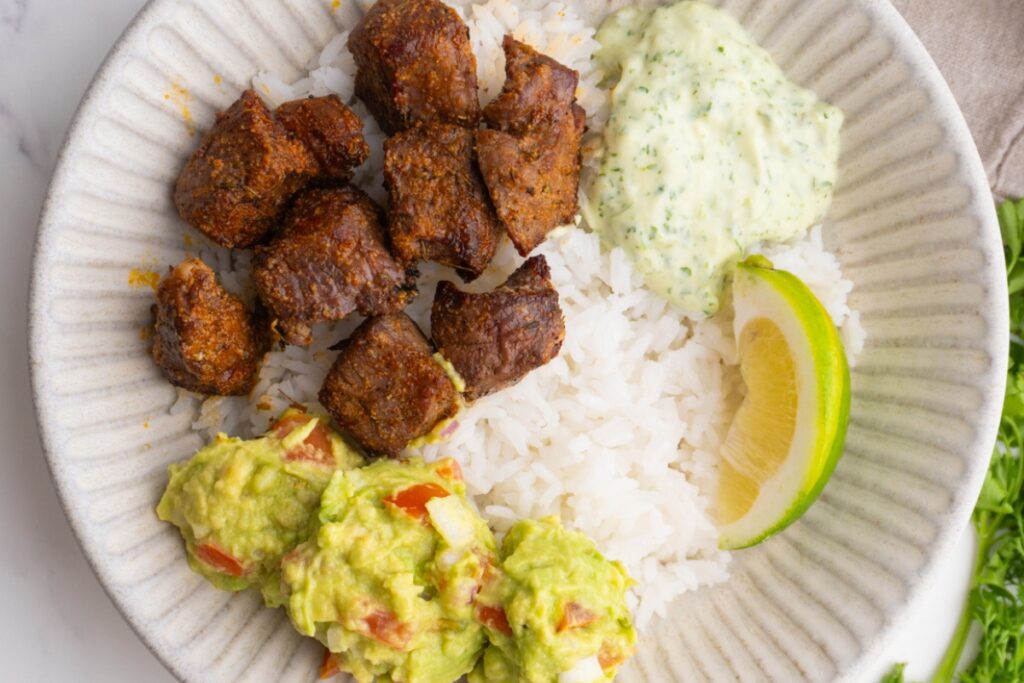 Close up of steak taco bowl with guacamole and cilantro jalapeño sauce.