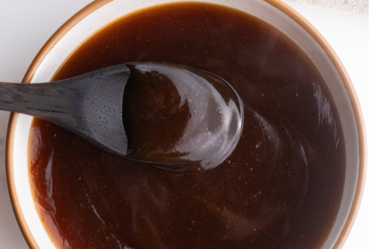 Close up of teriyaki sauce in a bowl with a small wooden spoon.