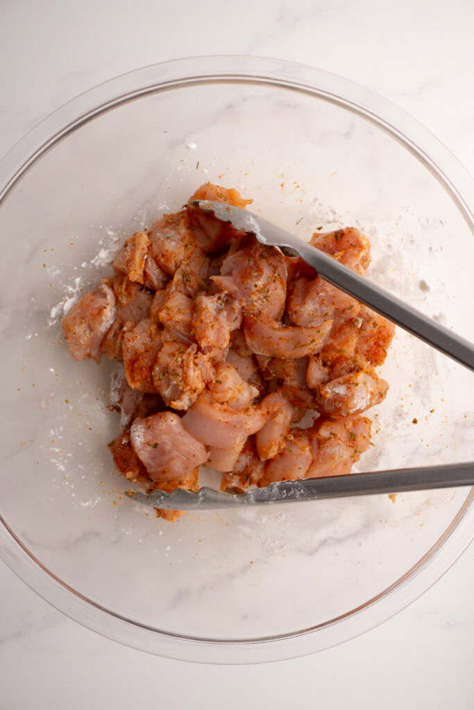 Chicken bites in a mixing bowl mixed with all the spices.