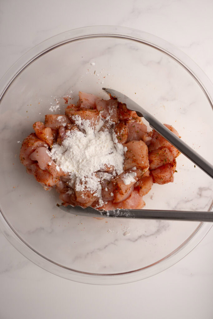 Cornstarch added to the seasoned chicken breast in a bowl.