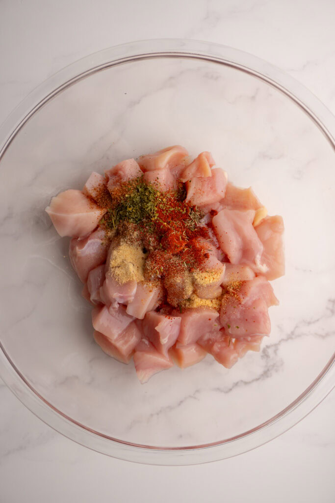 Spices added to diced chicken breast in a bowl.