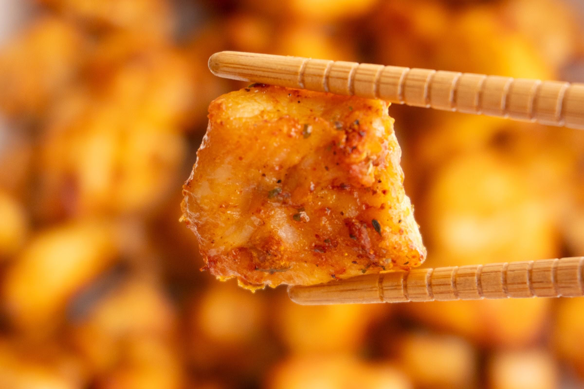 Close up of an air fryer chicken bite being held by chopsticks.