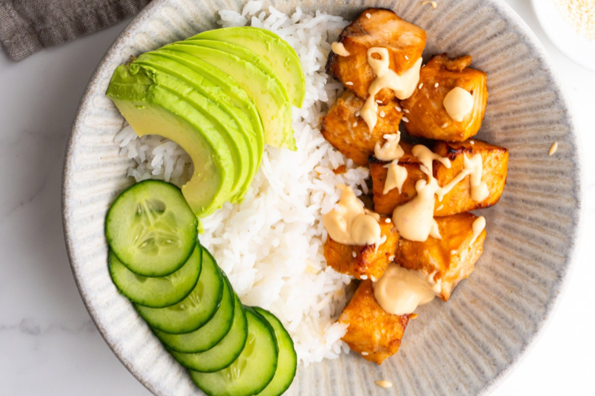 Close up of an air fryer salmon bowl with cucumber and avocado.