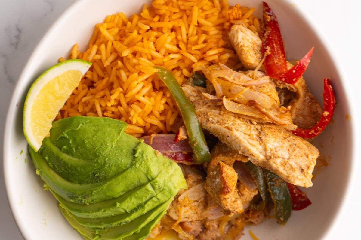 Close up of a chicken fajita bowl with avocado and lime.