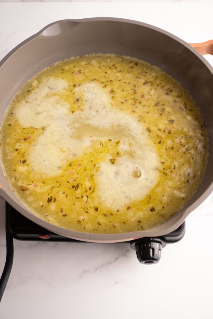Chicken stock starting to simmer in a skillet.