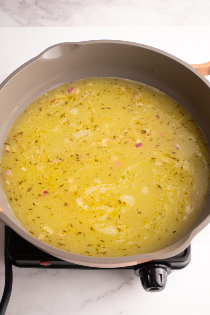 Chicken broth added to the shallots and butter mixture in a skillet.