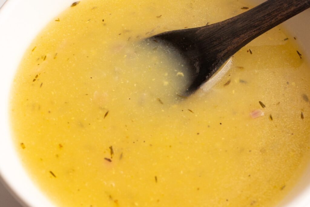 Close up of chicken stock gravy in a bowl with a small spoon.