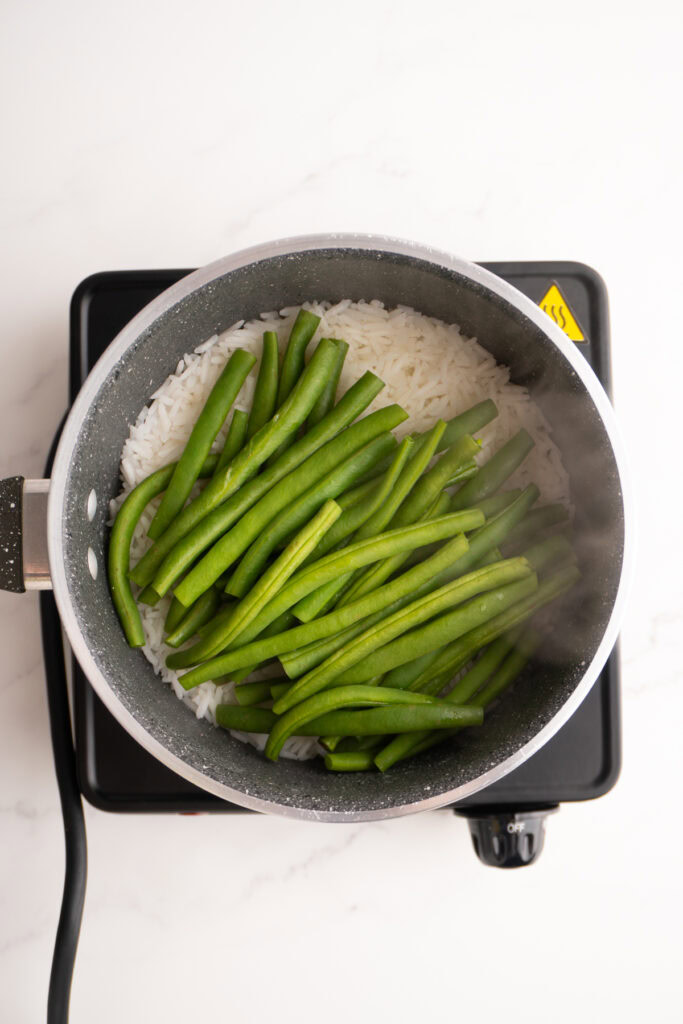 White rice with steamed green beans on top.