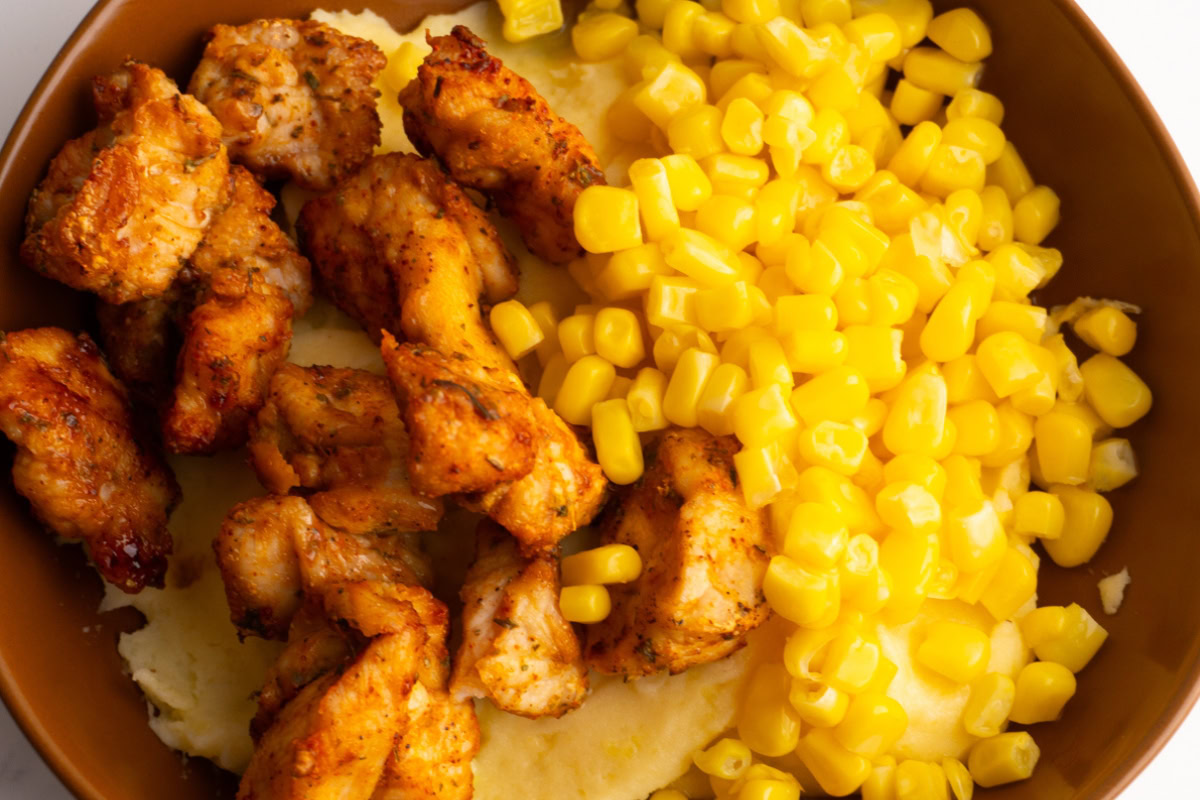 Close up of a mashed potato bowl with chicken and corn.