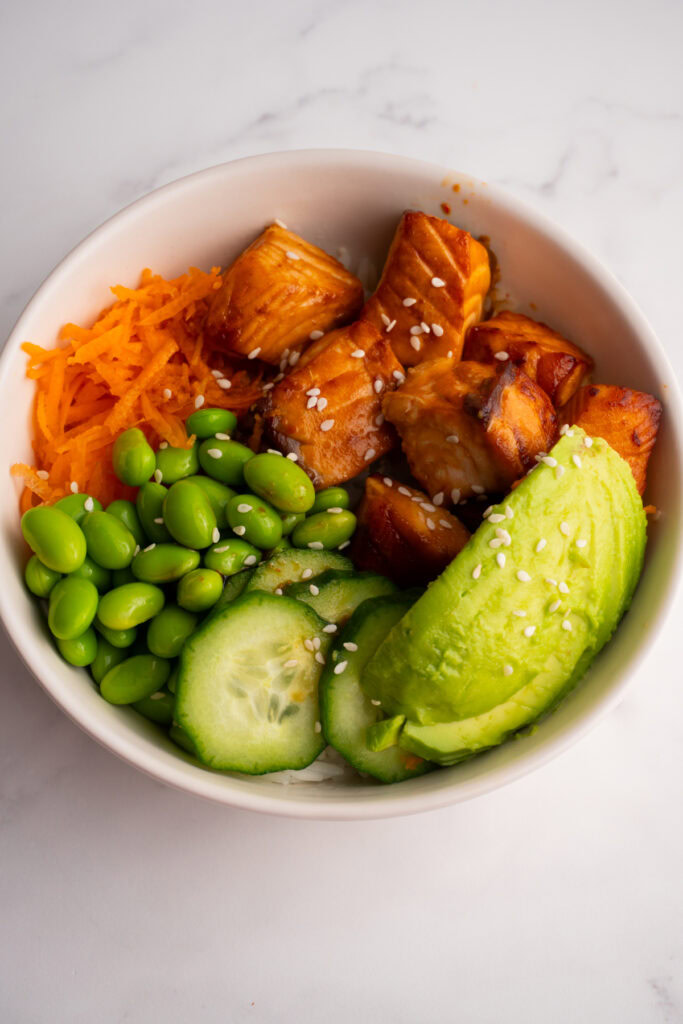 Cooked salmon poke bowl with avocado, edamame, and shredded carrots.