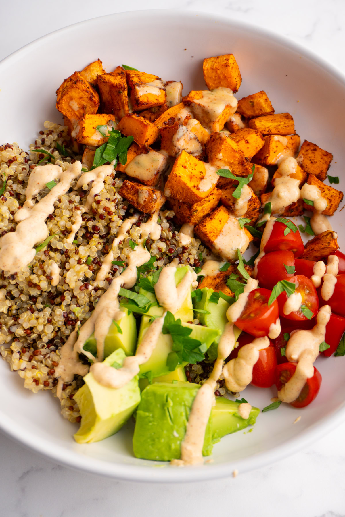 Sweet potato taco bowl with sweet potatoes, quinoa, cherries, avocado and taco sauce on top.
