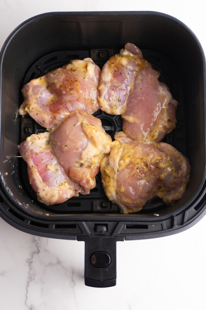 Chicken thighs in the air fryer basket before cooking.