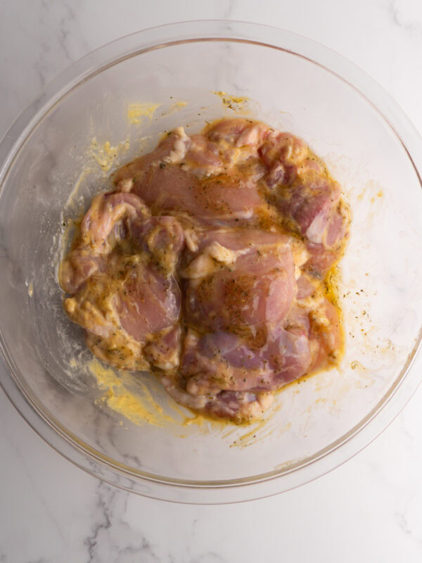 Chicken thighs in a glass bowl mixed with the honey mustard marinade.
