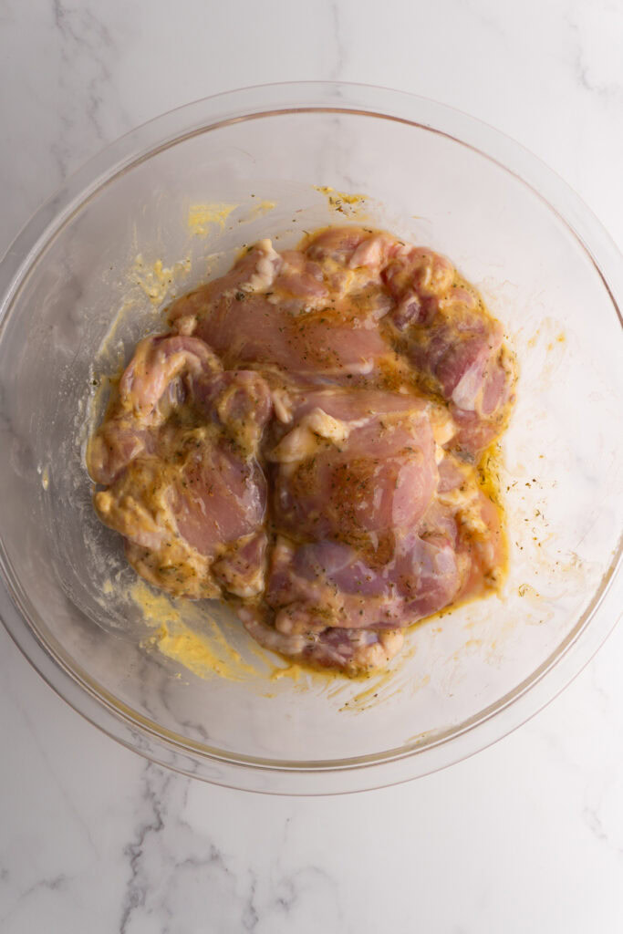 Chicken thighs in a glass bowl mixed with the honey mustard marinade.