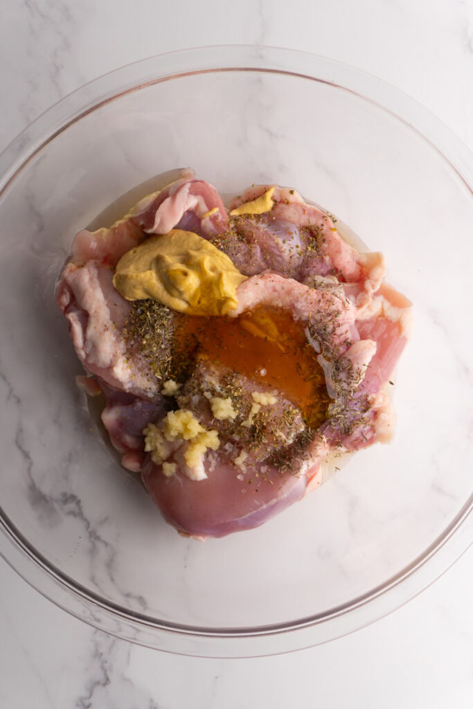 Chicken thighs in a bowl with honey mustard marinade ingredients on top.