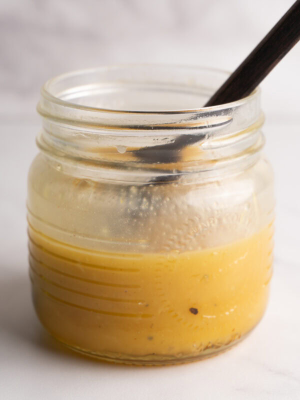 Side view of a jar of honey dijon vinaigrette with a spoon in the jar.