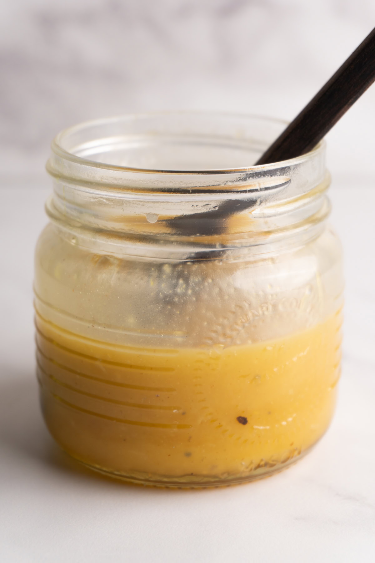Side view of a jar of honey dijon vinaigrette with a spoon in the jar.