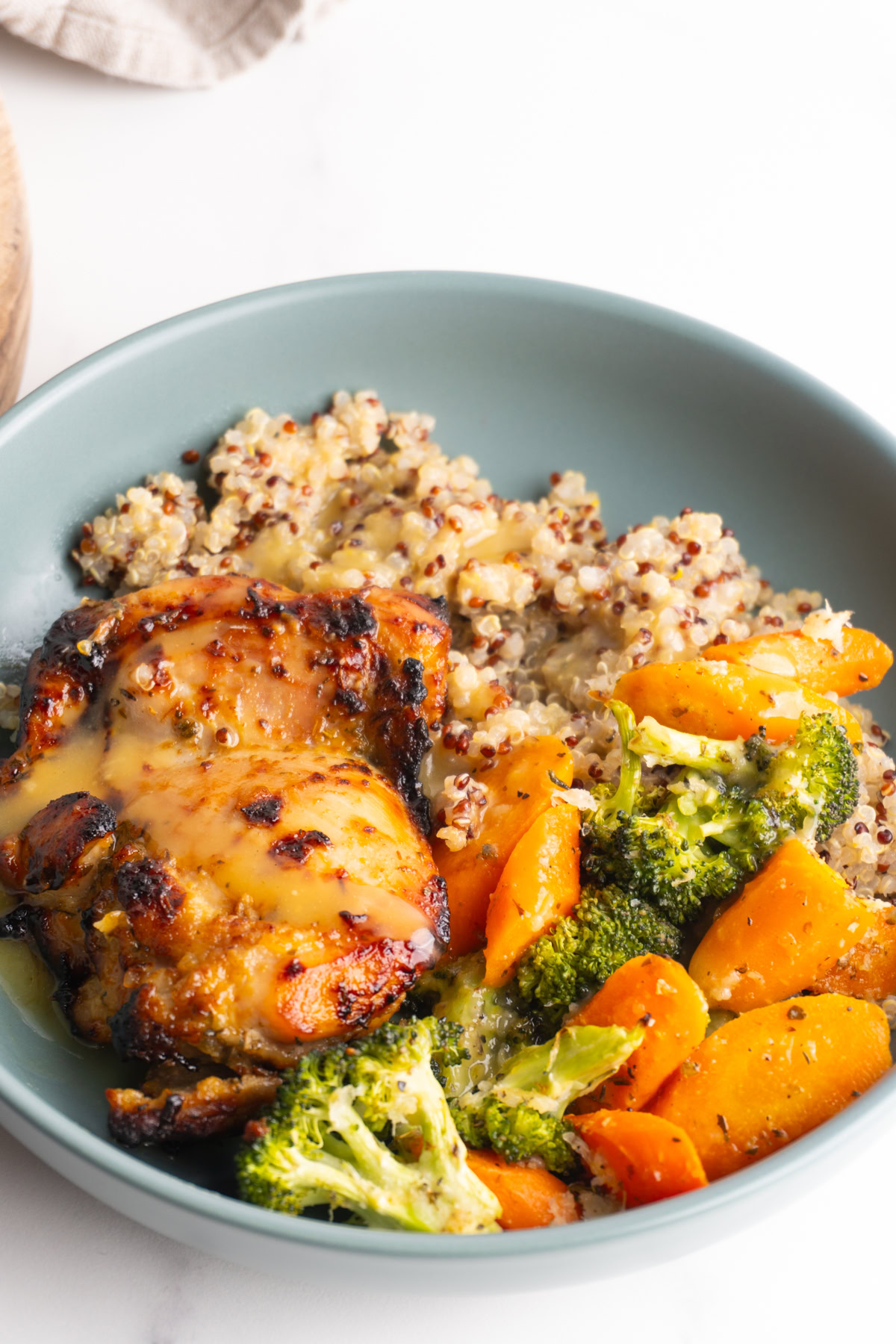 Honey mustard chicken thigh served with quinoa and roasted veggies in a bowl.