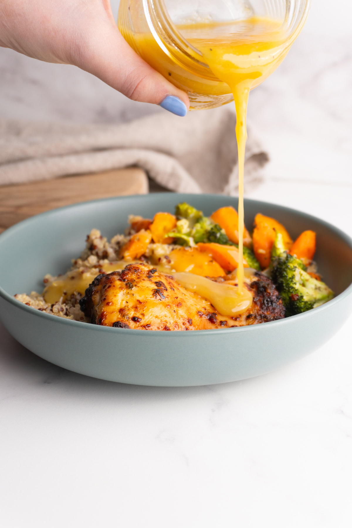 Pouring honey dijon vinaigrette over a bowl of quinoa, veggies and chicken.
