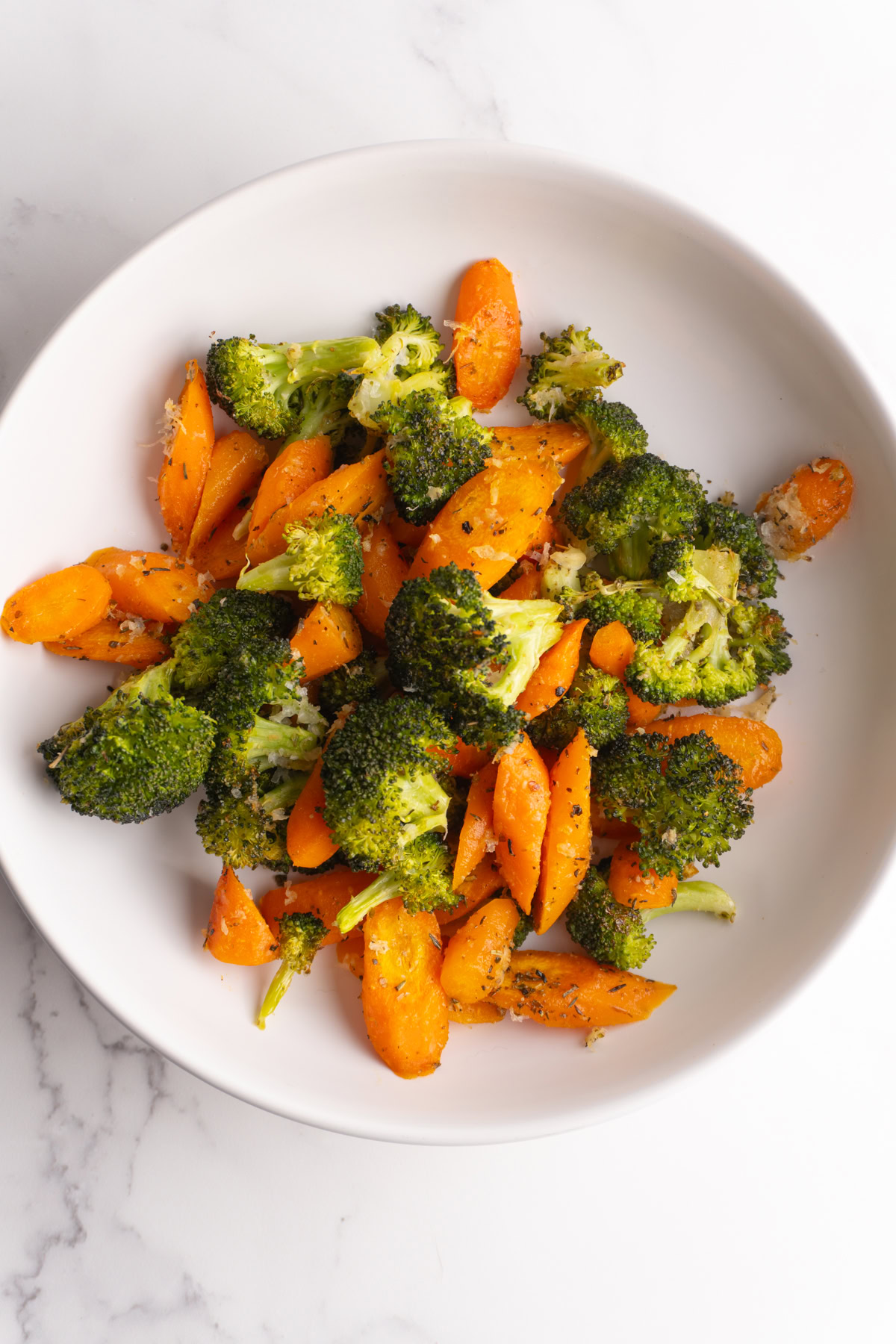Overhead shot of oven roasted broccoli and carrots in a white bowl.