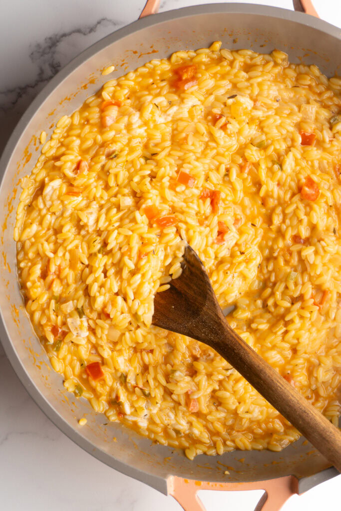 Finished creamy cajun orzo in a skillet with a wooden spoon.
