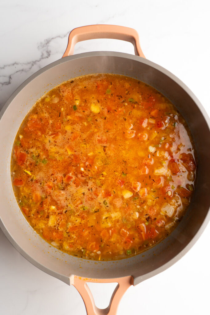Chicken broth with orzo in a skillet to cook.