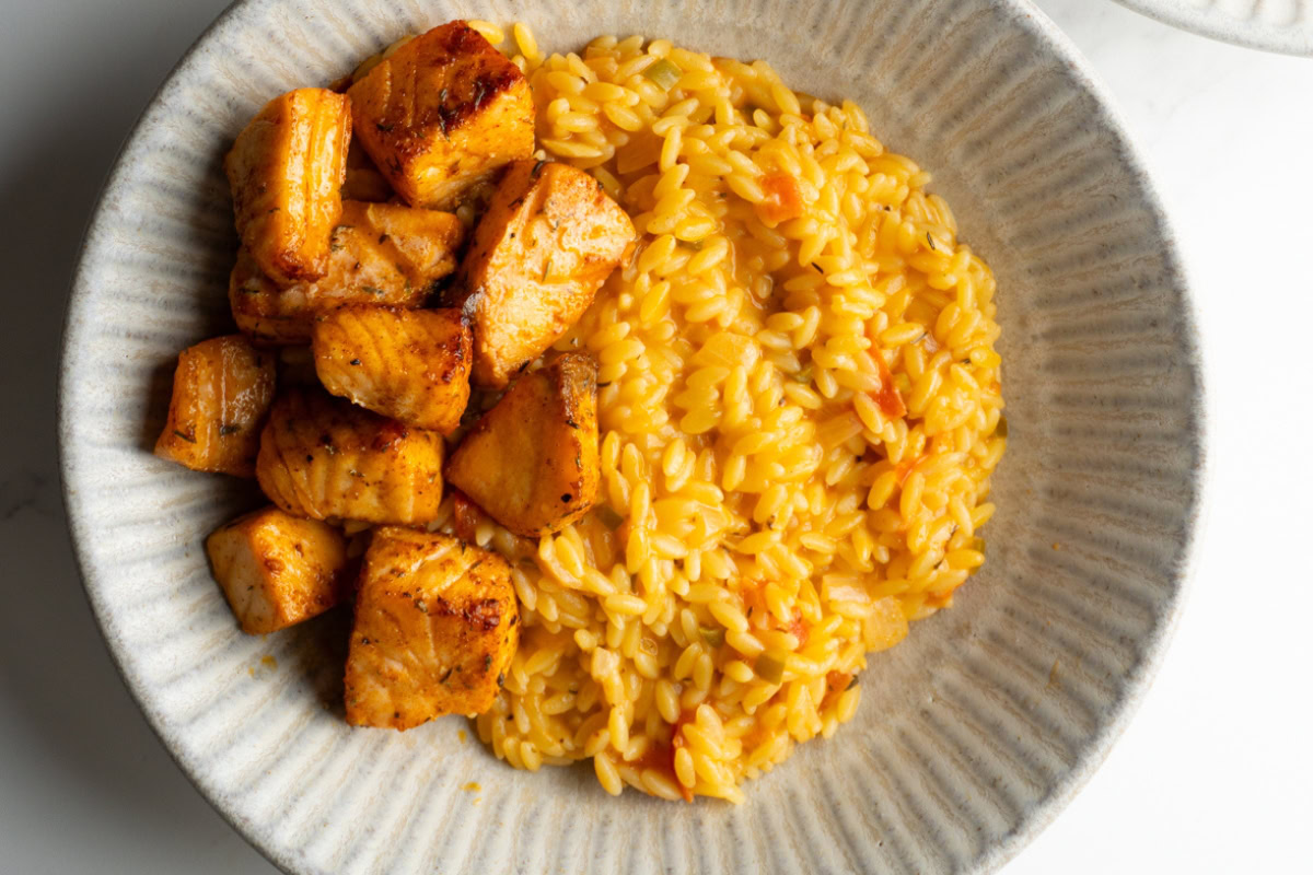 Cajun orzo served in a bowl with salmon bites on the side.