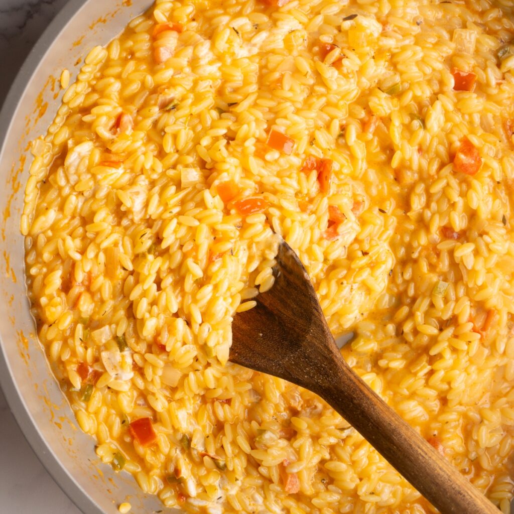 Close up of creamy cajun orzo in a skillet with a wooden spoon.