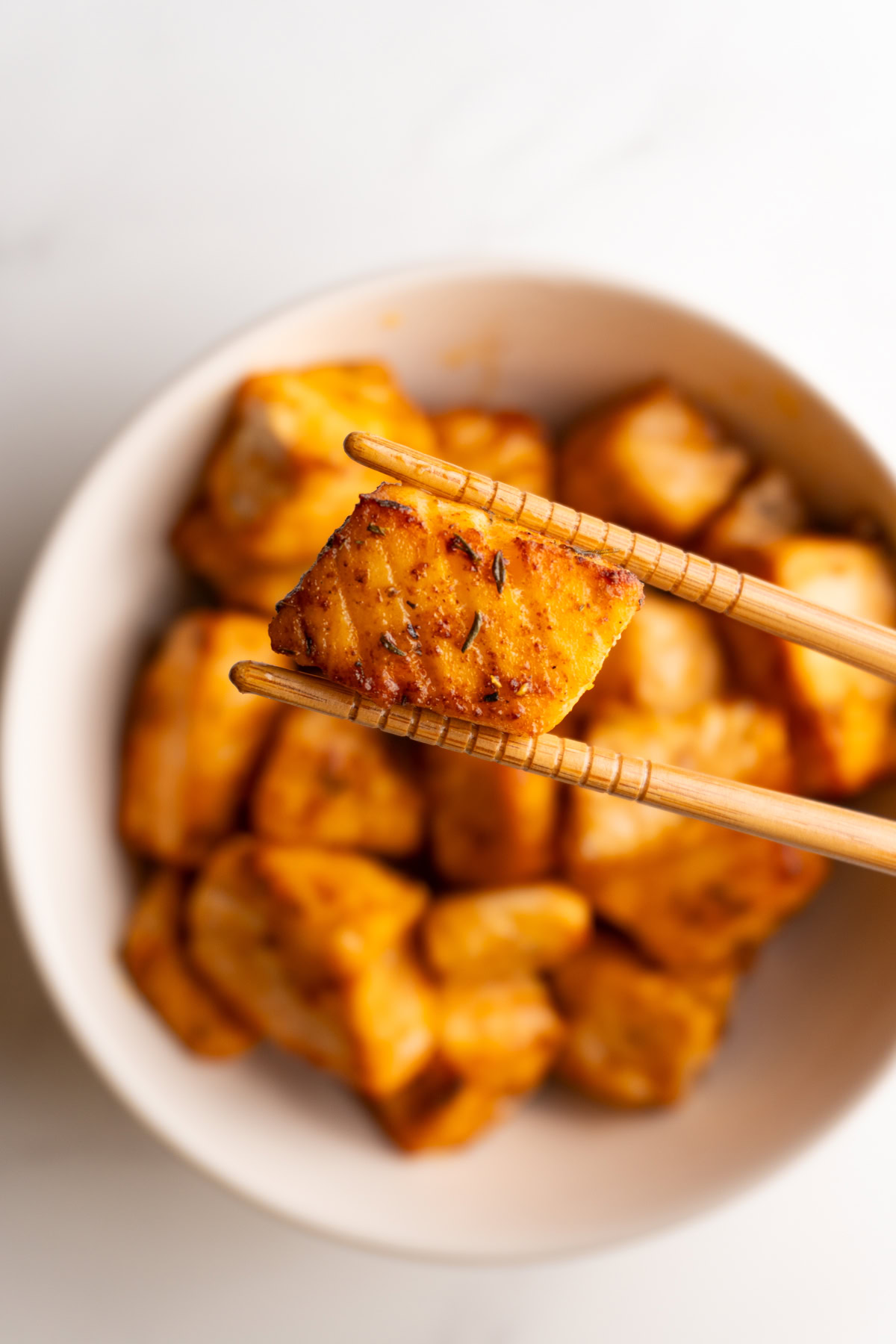 Chopsticks holding up a Cajun salmon bite hovering over a bowl of the other salmon bites.