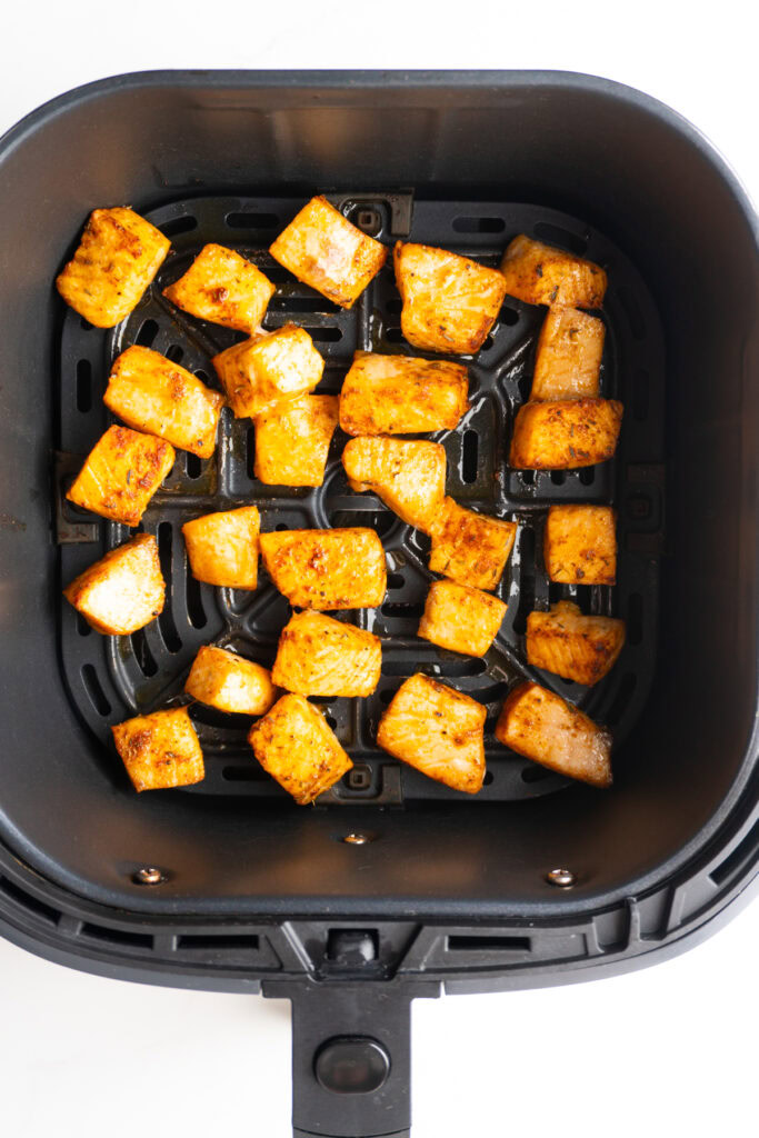 Air fryer cajun salmon bites in the air fryer basket after cooking.