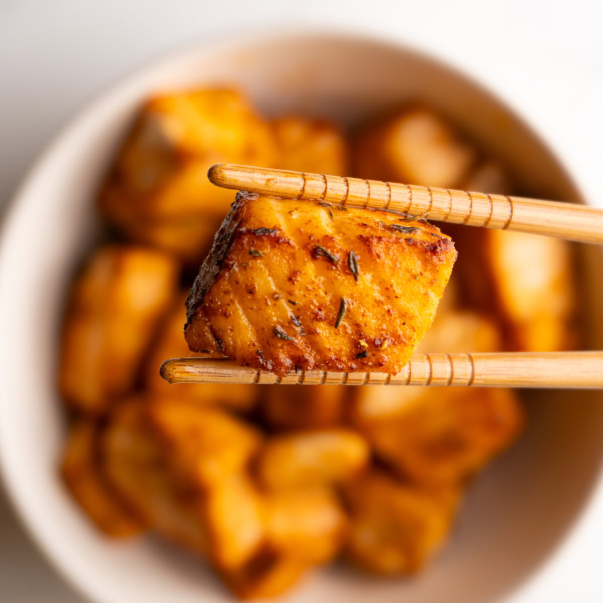 Cajun salmon bite being held by chopsticks hovering over a bowl of salmon bites.