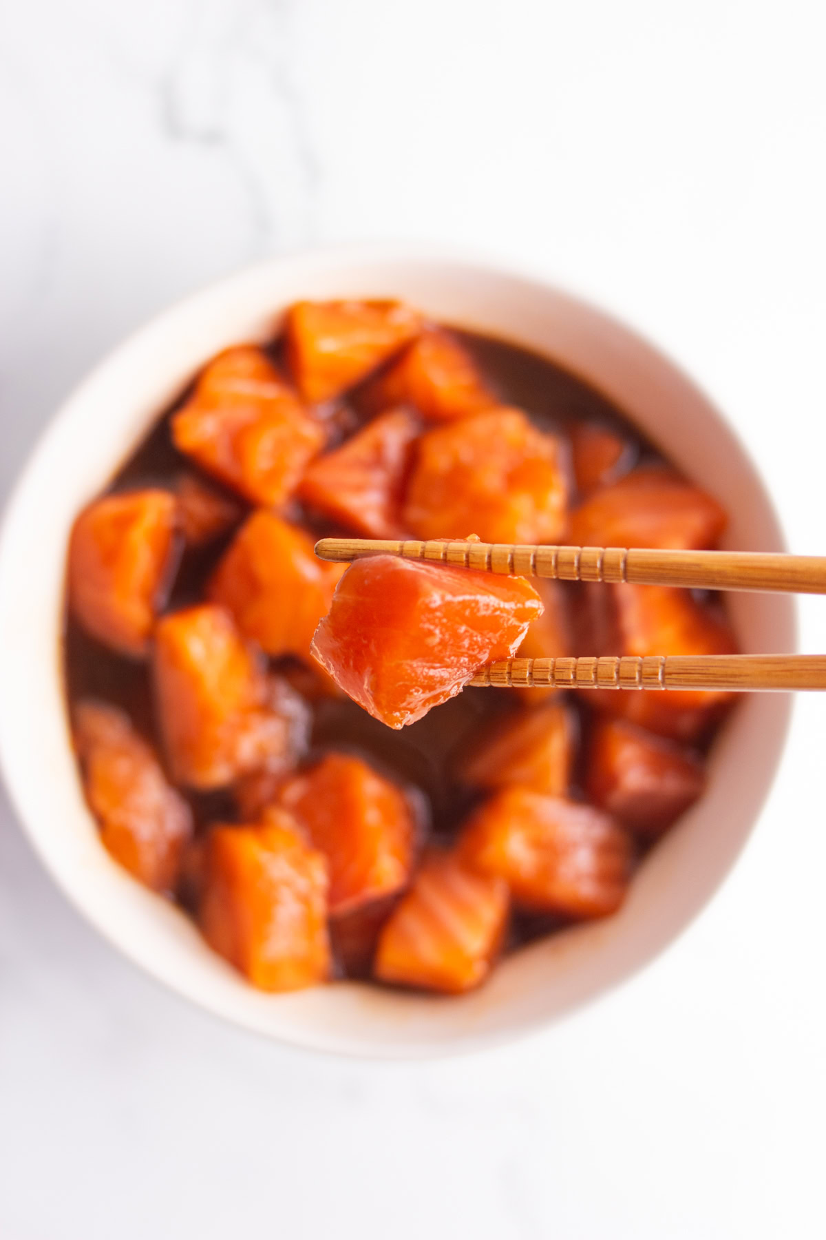 Holding a piece of fresh salmon with chopsticks hovering over salmon in poke sauce.