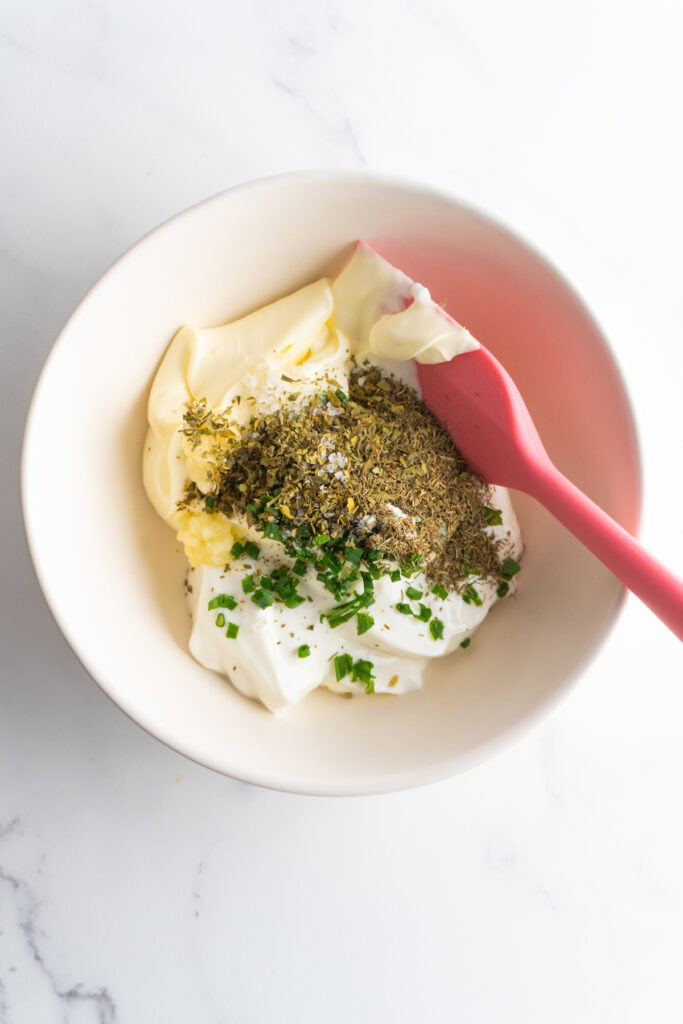 Sour cream and Greek yogurt with spices and chives in a bowl before combining.