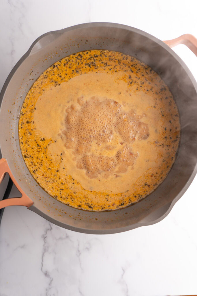 Heavy cream added to the marry me sauce in a skillet.