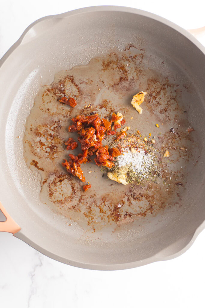 Spices, garlic, and sun dried tomatoes in a skillet to cook.