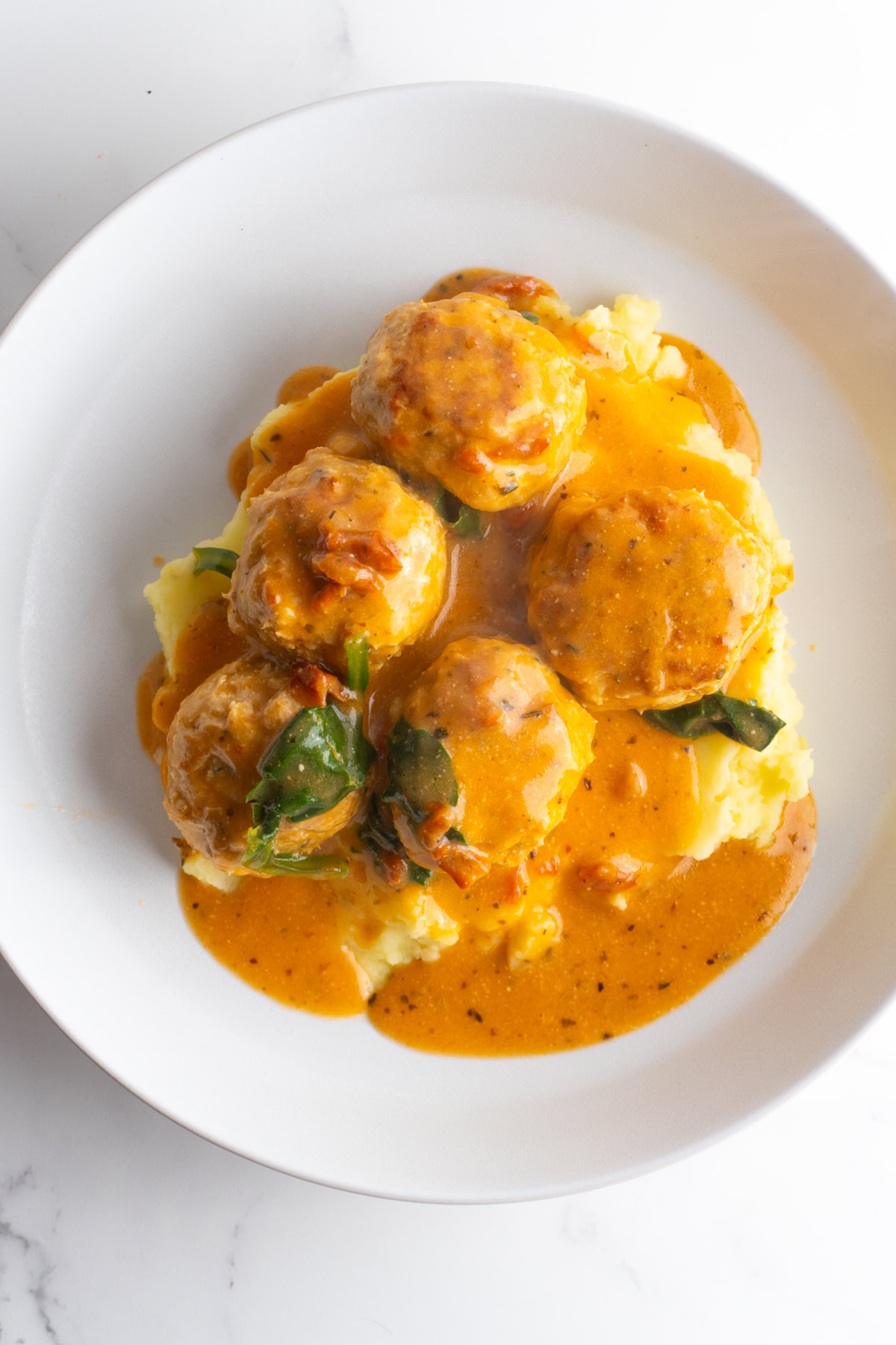 Overhead shot of marry me chicken meatballs on a bed of mashed potatoes on a plate.