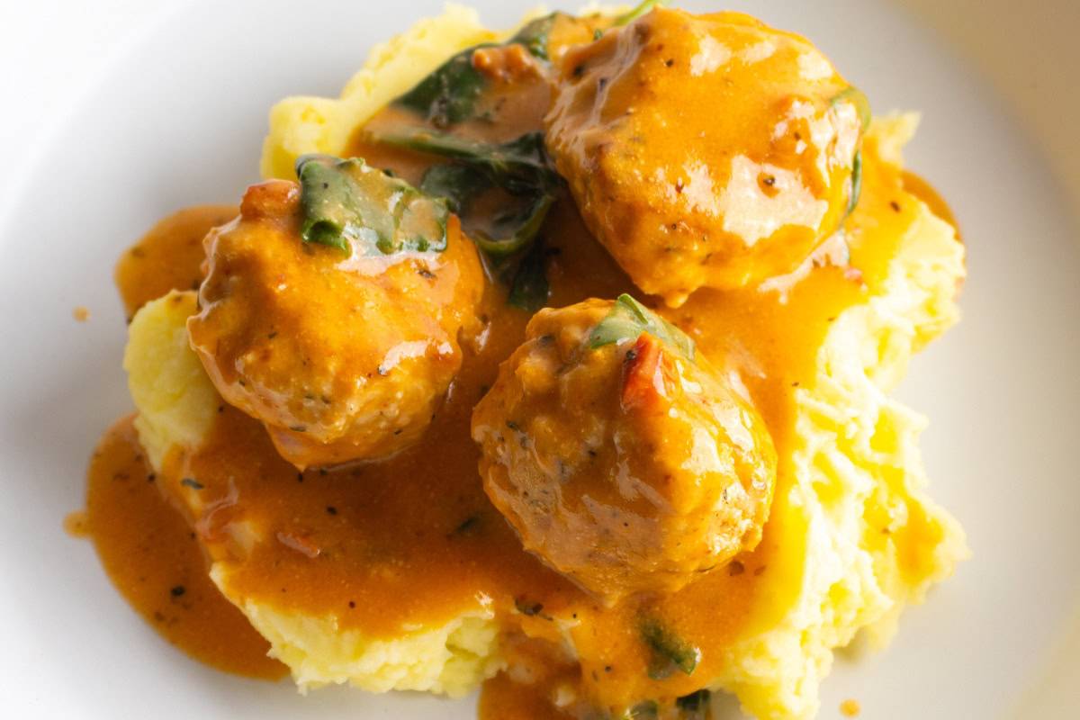 Marry me chicken meatballs on a bed of mashed potatoes in a bowl.