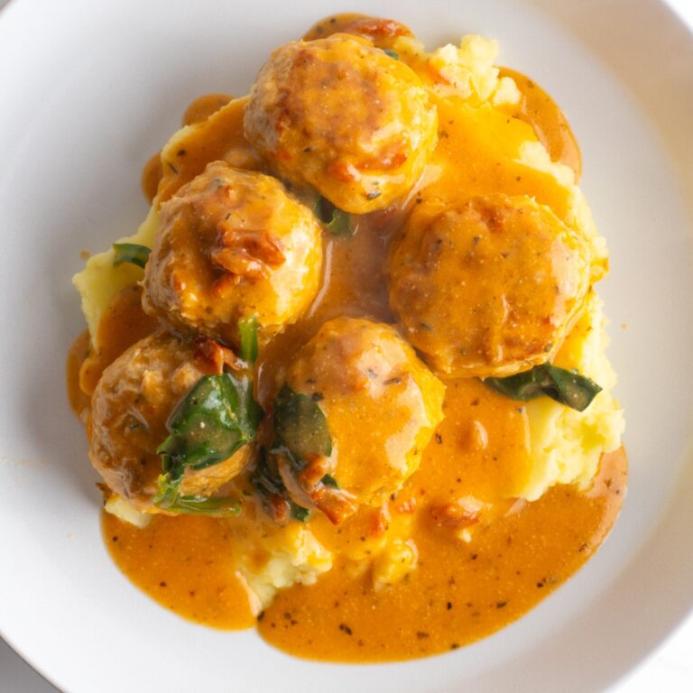 Close up of marry me chicken meatballs on a bed of mashed potatoes.