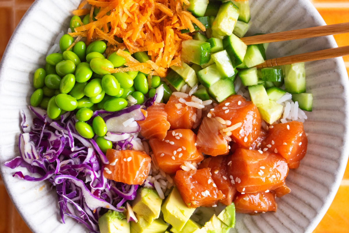 Close up of salmon poke bowl with toppings and chopsticks.