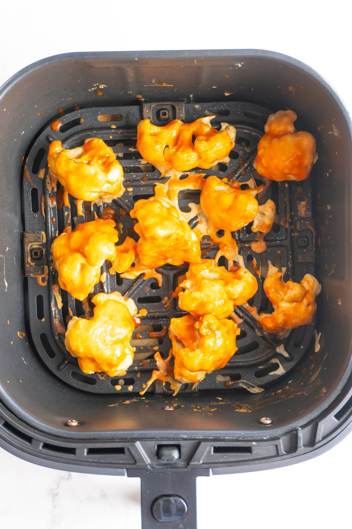 Cauliflower in an air fryer with buffalo sauce on them.