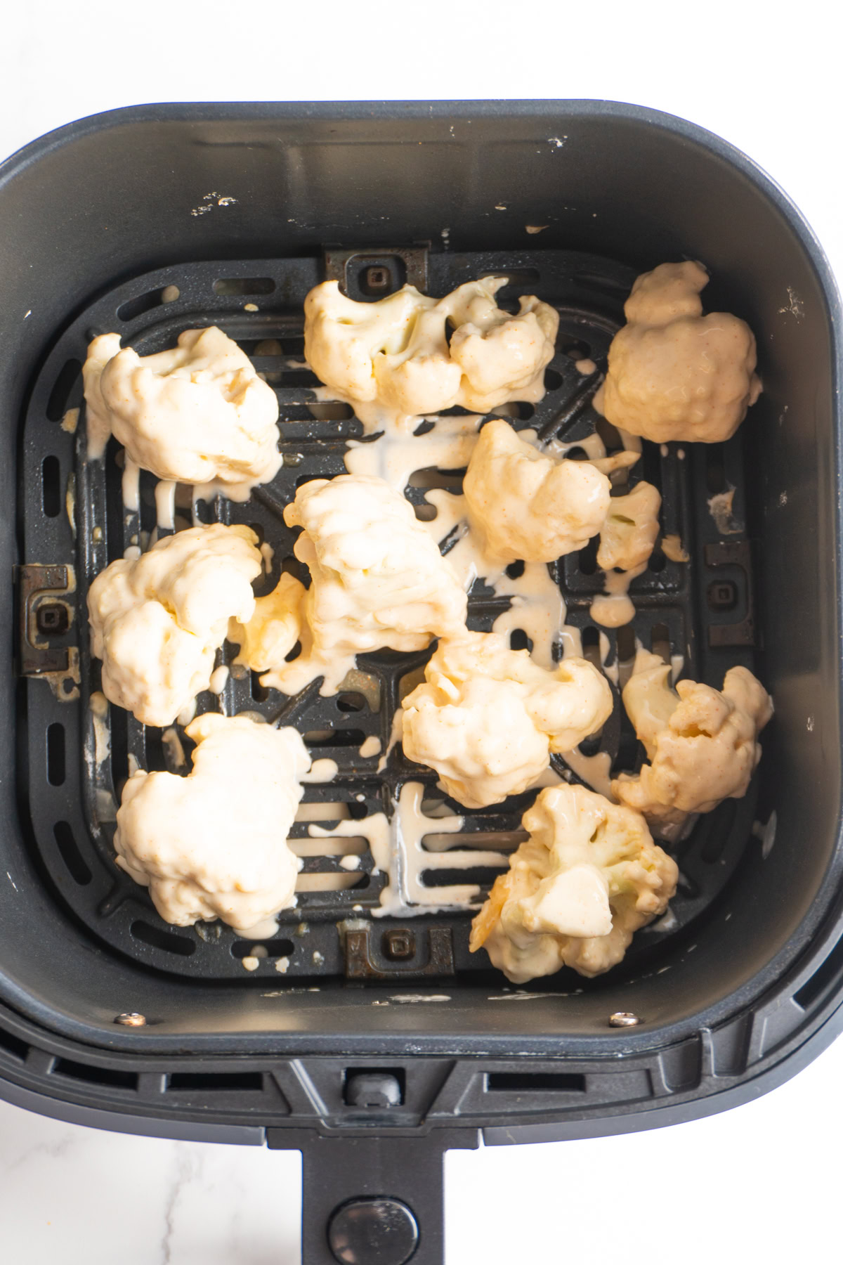 Cauliflower dipped in batter placed in an air fryer.