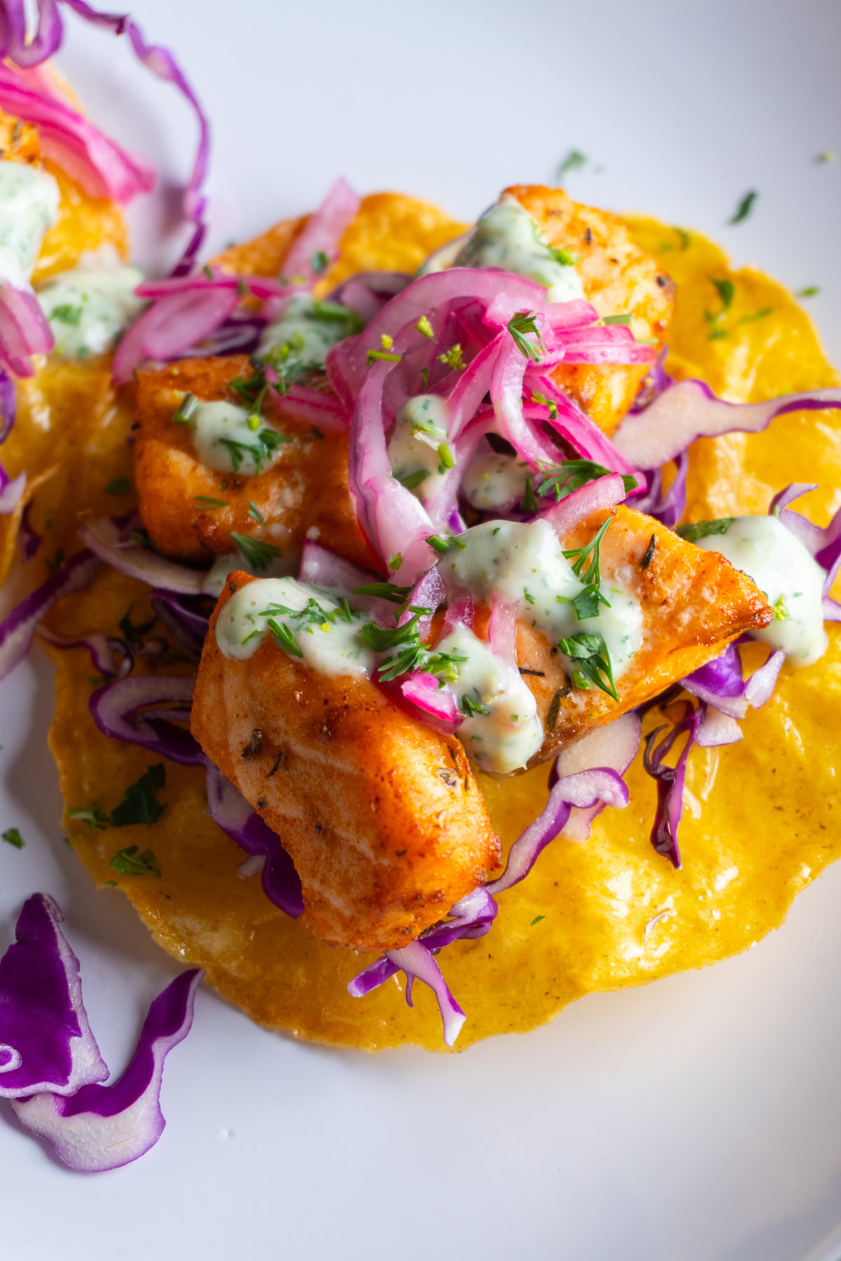 Salmon tostada on a plate with cabbage, pickled onions, cilantro ranch on top.