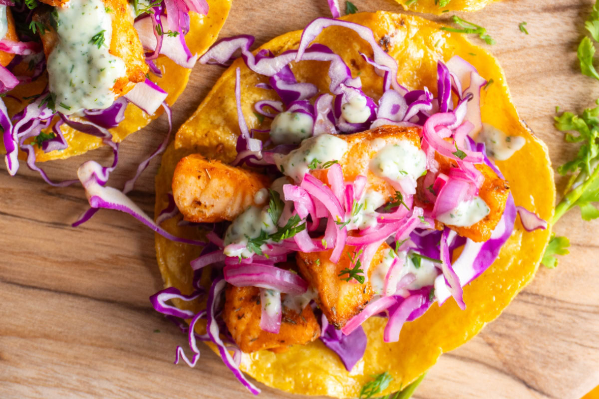 Salmon tostada with toppings like cabbage, onions, and cilantro ranch.