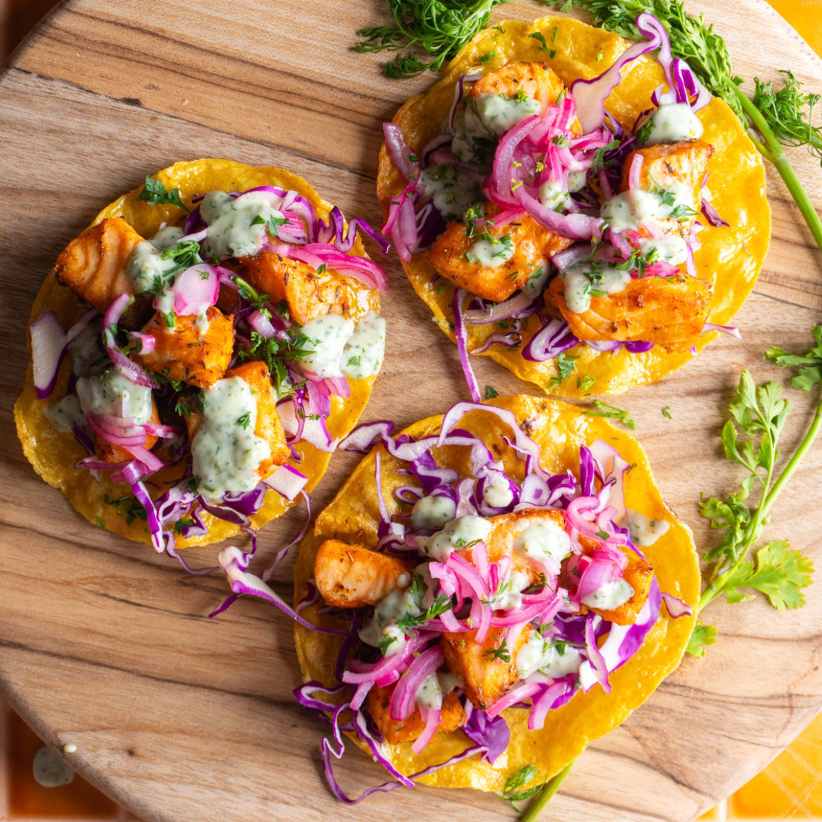 Overhead shot of three salmon tostadas on a wooden board.