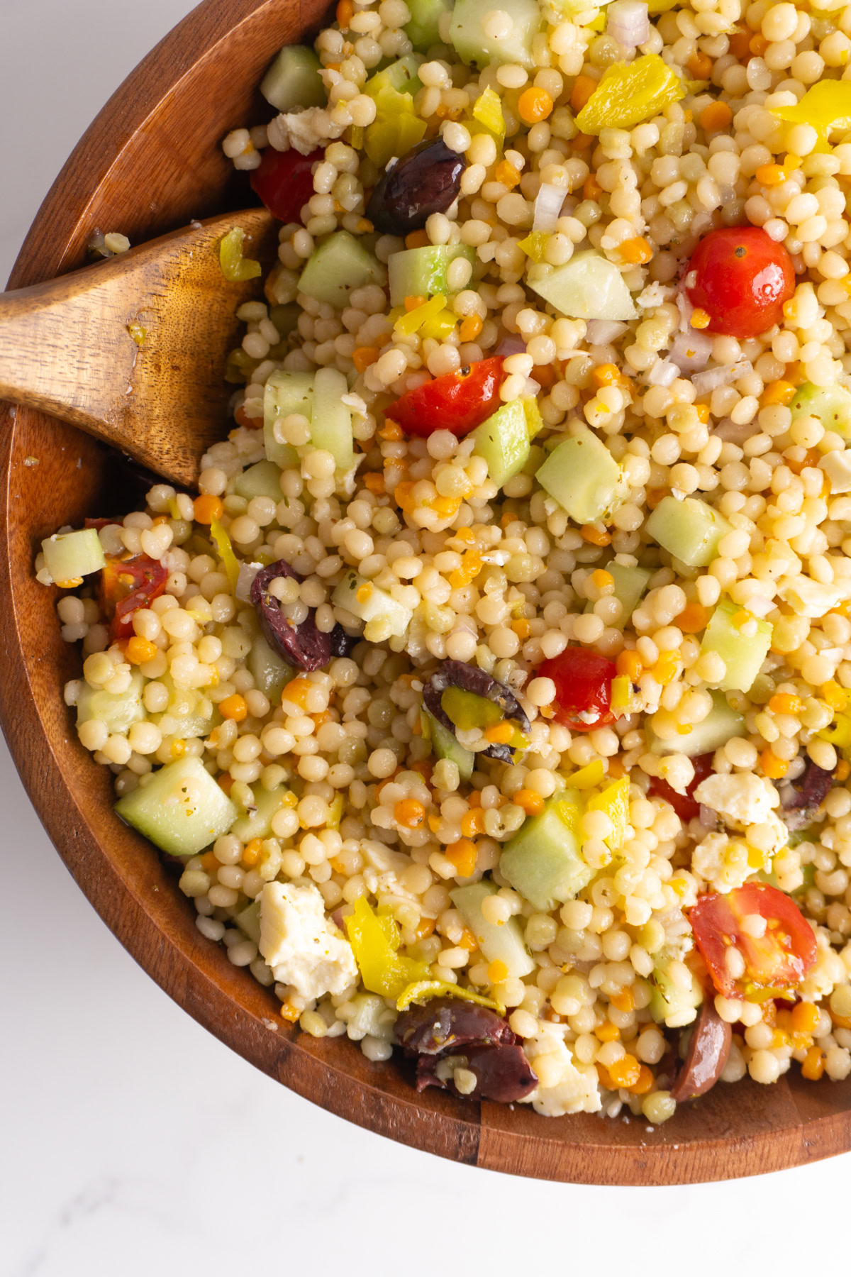 Greek couscous salad in a wooden salad bowl with a wooden spoon.