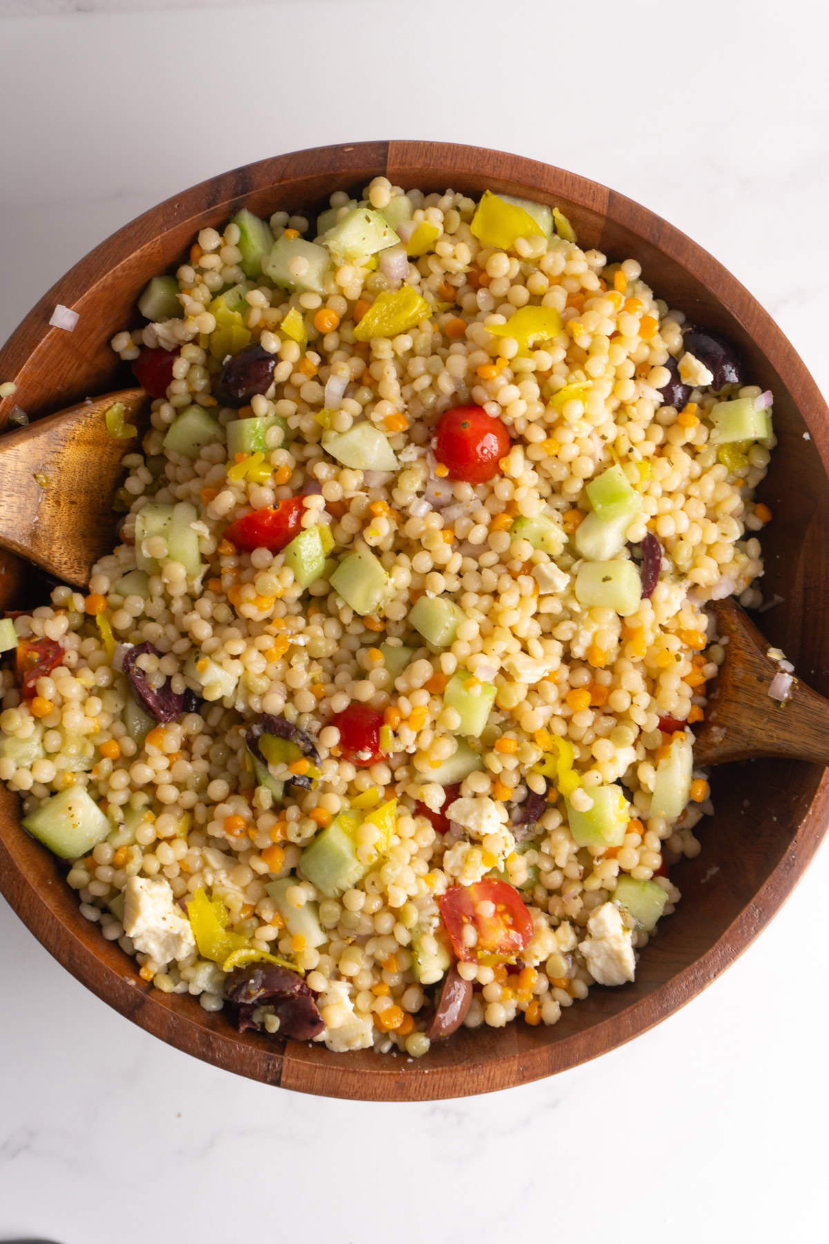 Mixed up Greek couscous salad in a wooden bowl.